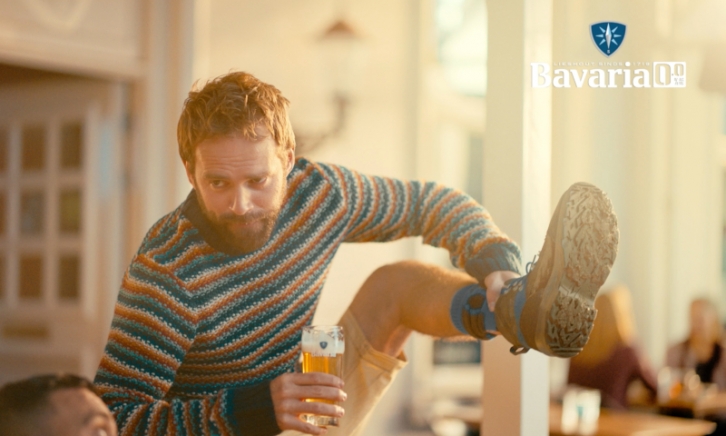 Man met een glas Bavaria 0.0% in de hand tilt zijn been op om zijn schoen te laten zien